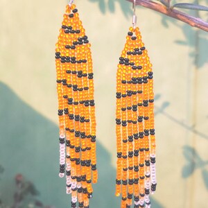 May include: A pair of long, beaded earrings with a tiger stripe pattern in orange, black, and white.