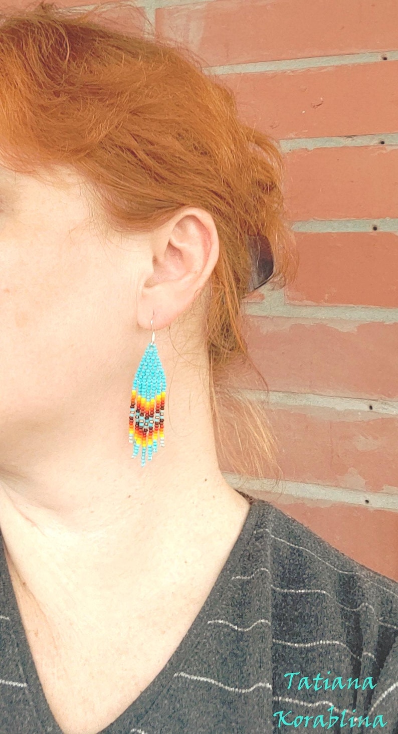 May include: A pair of turquoise, red, orange and yellow beaded earrings. The earrings are teardrop shaped and hang from silver hooks.