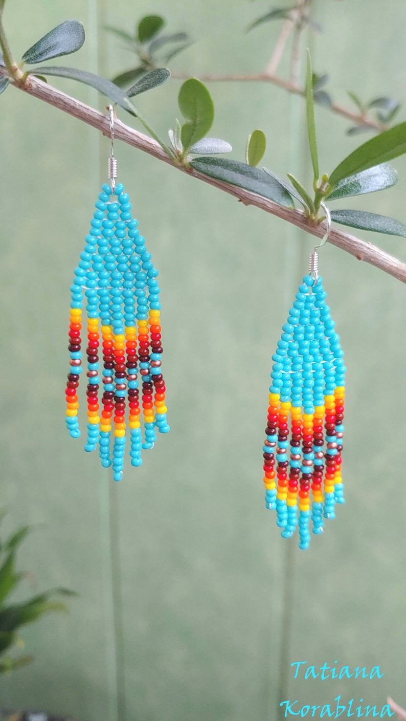 May include: A pair of turquoise beaded earrings with red, orange and yellow accents. The earrings are hanging from a branch.