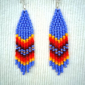 May include: A pair of blue, orange, red and yellow beaded dangle earrings. The earrings are made with small seed beads and have a fringe-like design.
