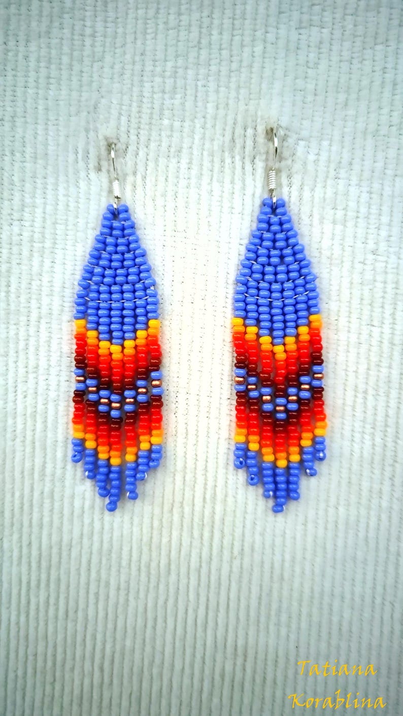 May include: A pair of blue, orange, red and yellow beaded dangle earrings. The earrings are made with small seed beads and have a fringe-like design.