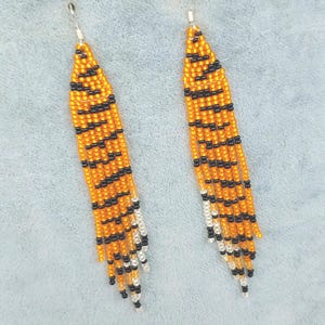 May include: A pair of long, beaded earrings with a tiger stripe pattern in orange, black, and white.