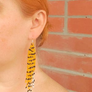 May include: A pair of long, beaded earrings with a tiger print pattern in yellow, black, and white.