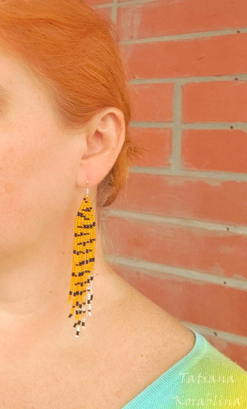 May include: A pair of long, beaded earrings with a tiger print pattern in yellow, black, and white.