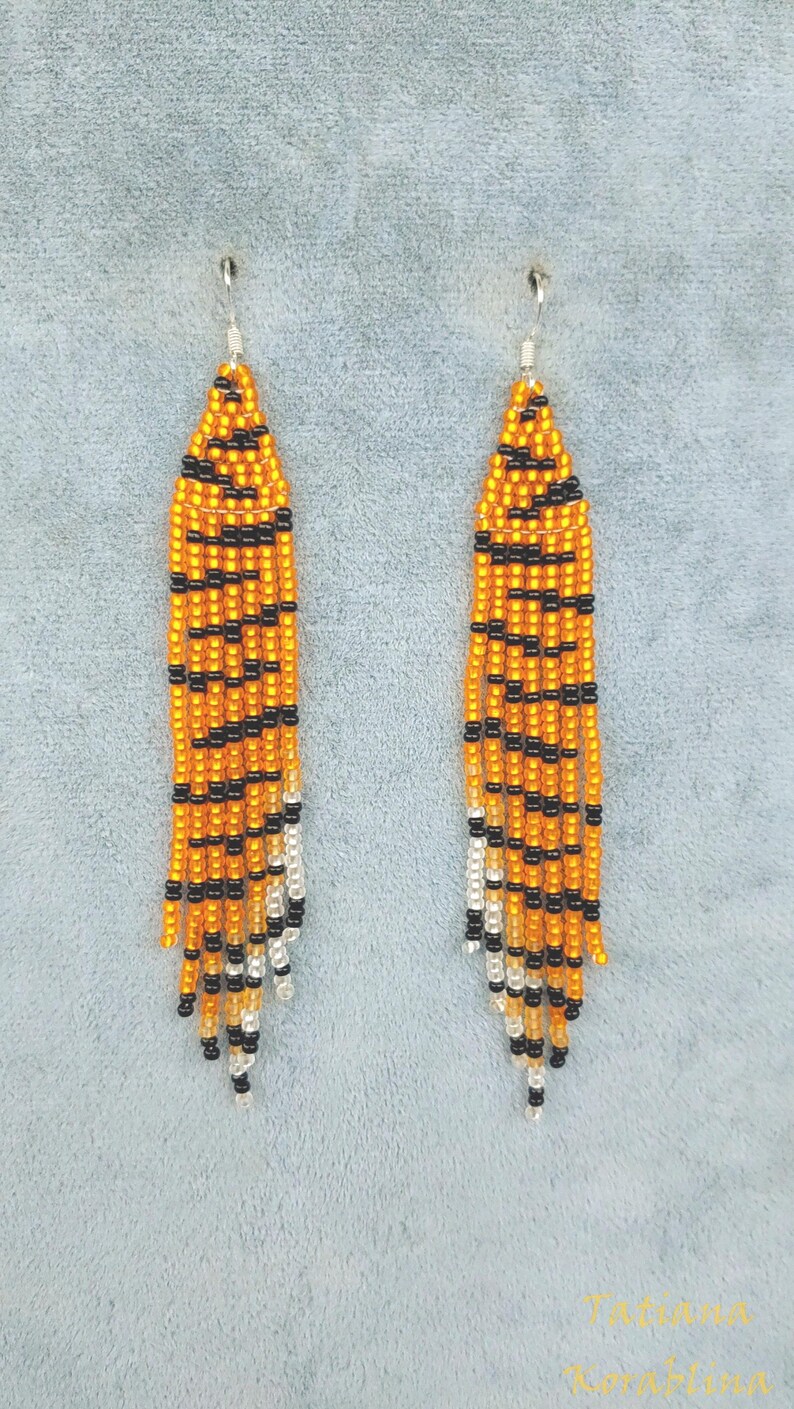 May include: A pair of long, orange and black beaded earrings with a white fringe. The earrings are made with small beads and have a tiger stripe pattern.