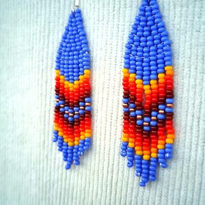 May include: A pair of blue, orange, red and yellow beaded earrings. The earrings are teardrop shaped and have a geometric pattern.