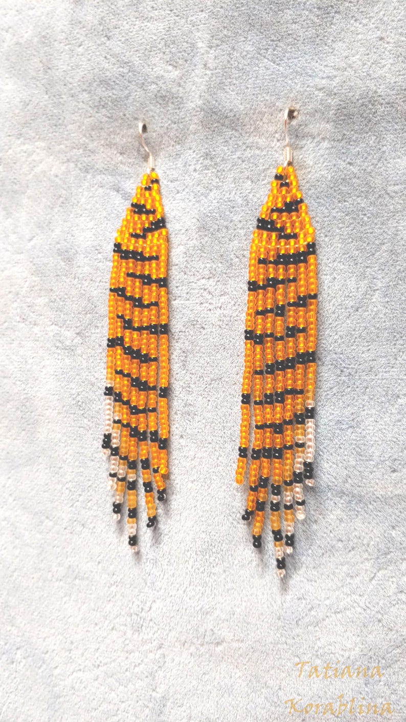 May include: A pair of long, beaded earrings with a tiger stripe pattern in orange and black. The earrings are made with small, round beads and have a silver hook closure.