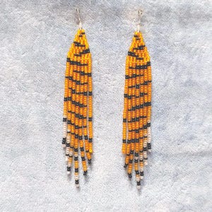 May include: A pair of long, beaded earrings with a tiger stripe pattern in orange, black, and white.