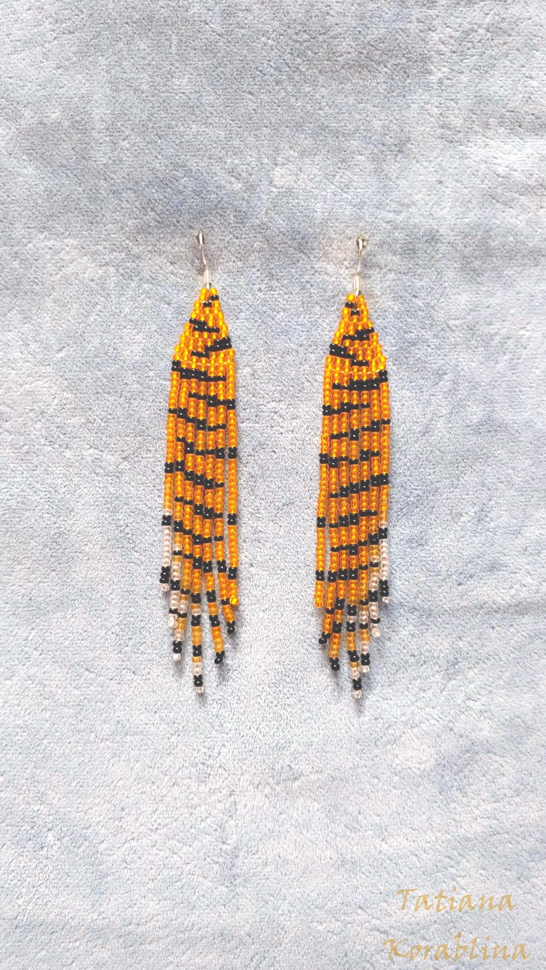 May include: A pair of long, beaded earrings with a tiger stripe pattern in orange, black, and white.