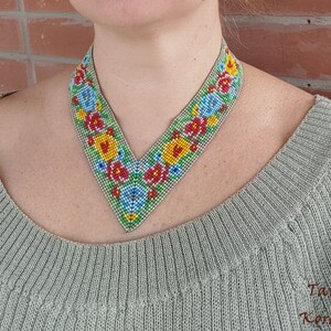 May include: A V-shaped beaded necklace with a floral pattern in shades of red, yellow, blue, and green. The necklace is made of small beads and has a delicate, intricate design.