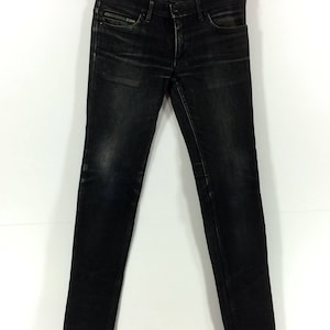 May include: Black skinny jeans with a zipper detail on the front pocket.