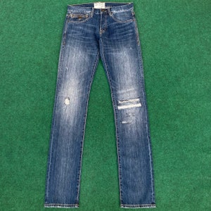 May include: Distressed blue denim jeans with a faded look and small rips on the knees. The jeans have a straight leg fit and a classic five-pocket style.