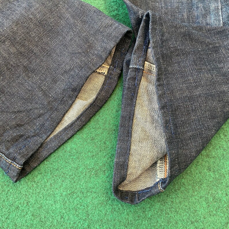 May include: Close-up of the inside of two denim pant legs, showing the raw edge of the fabric and the stitching.