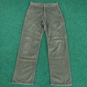 Può includere: Pantaloni cargo verde oliva con design a gamba dritta. I pantaloni presentano dettagli borchiati lungo le cuciture laterali e intorno alla tasca cargo. Hanno un classico design a cinque tasche.