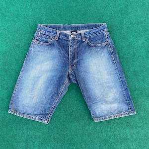 Puede incluir: Pantalones cortos de mezclilla azul con un lavado descolorido y cierre de botón.