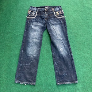 May include: Distressed blue denim jeans with decorative stitching and a brand label on the waistband.