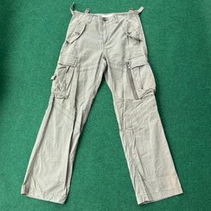 Könnte beinhalten: Eine hellgraue Cargohose mit mehreren Taschen und Reißverschlussdetails.