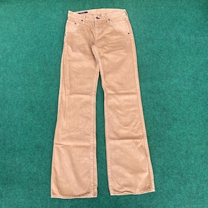 May include: Tan corduroy trousers with a classic five-pocket design. The trousers have a button and zip closure and a flared leg. The fabric appears soft and has a subtle texture. The trousers are displayed on a green surface.
