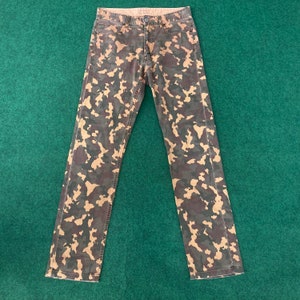 May include: Camouflage print jeans with a brown, tan, and green color scheme.