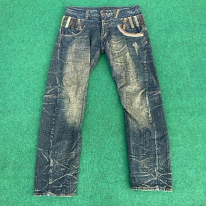 Puede incluir: Vaqueros de mezclilla azul desgastados con una cintura estampada en marrón y multicolor.