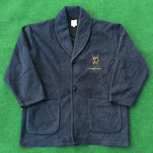 May include: A navy blue fleece robe with a gold embroidered logo that says "Jean-Paul Gaultier" on the front. The robe has a shawl collar and a button closure.