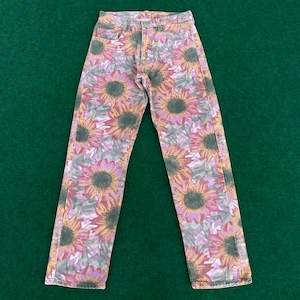 May include: A pair of light blue denim jeans with a sunflower print. The print is in shades of pink, purple, and brown.