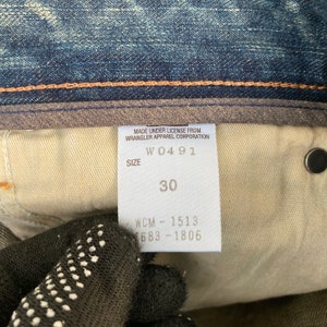 May include: A white tag with black text that reads "Made under license from Wrangler Apparel Corporation" and "Size W0491 30 WCM - 1513 1683 - 1806".