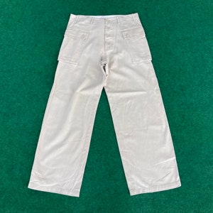 May include: A pair of beige utility trousers with large cargo pockets and a button fly.