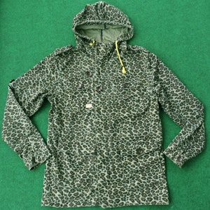 Könnte beinhalten: Eine grüne und braune Jacke mit Kapuze im Leopardenmuster und einem gelben Reißverschluss.