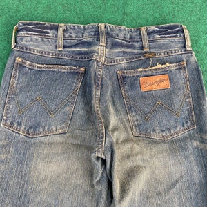 May include: A pair of blue denim jeans with a brown leather patch that says "Wrangler" on the back pocket.
