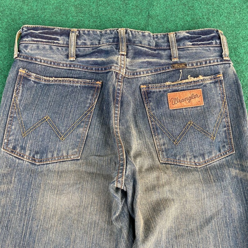 May include: A pair of blue denim jeans with a brown leather patch that says "Wrangler" on the back pocket.