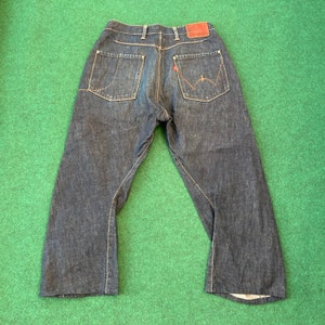 May include: A pair of dark blue denim jeans with a straight leg and a wide, relaxed fit. The jeans have a brown leather patch on the back waistband.