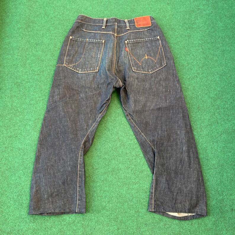 May include: A pair of dark blue denim jeans with a straight leg and a wide, relaxed fit. The jeans have a brown leather patch on the back waistband.
