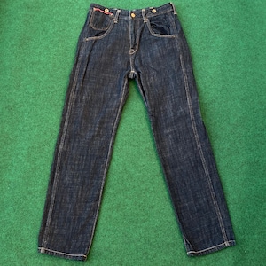 May include: Dark wash denim jeans with a classic five-pocket design. The jeans have a straight leg cut and feature a button and zipper closure. The pockets have a red accent. The jeans are displayed on a green surface.