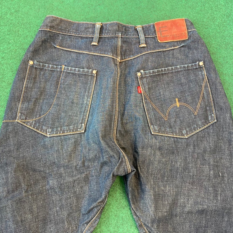 May include: A pair of dark blue denim jeans with a brown leather patch on the back waistband that says "Functional Control".