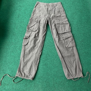 Puede incluir: Pantalón cargo gris con múltiples bolsillos y un cordón en la parte inferior.