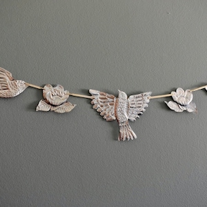 May include: A white paper garland with a string of birds and flowers. The birds are in flight and the flowers are in bloom. The garland is perfect for a party or special occasion.