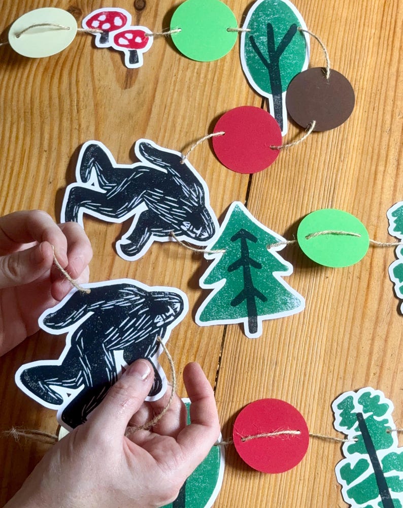 May include: A handmade woodland-themed garland featuring black animal silhouettes, red mushrooms, green trees, and red and green circles strung on twine. The garland is designed for festive decorations.
