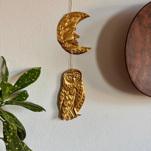 May include: A gold metal owl and crescent moon hanging mobile. The owl is detailed with feathers and the moon has a face.
