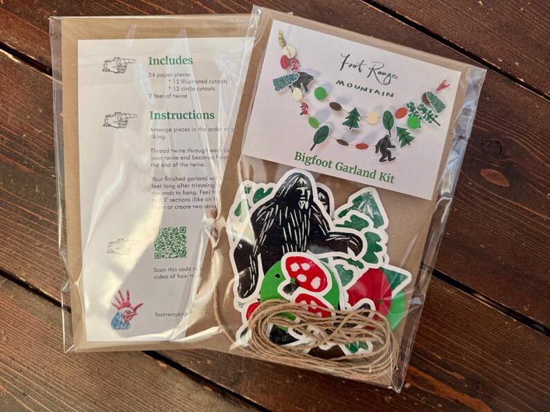 May include: A Bigfoot Garland Kit in a clear plastic package. The kit includes paper pieces, twine, and instructions. The package features a Bigfoot illustration, trees, and mushrooms. The text "Foot Range Mountain Bigfoot Garland Kit" is visible.