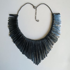 May include: A black metal necklace with a fan-shaped design. The necklace is made of many small, thin metal pieces that are connected together.