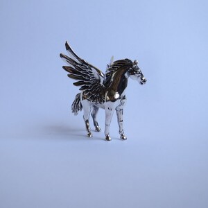 May include: A silver figurine of a winged horse, with a detailed sculpted body and wings. The horse is standing on a white background.