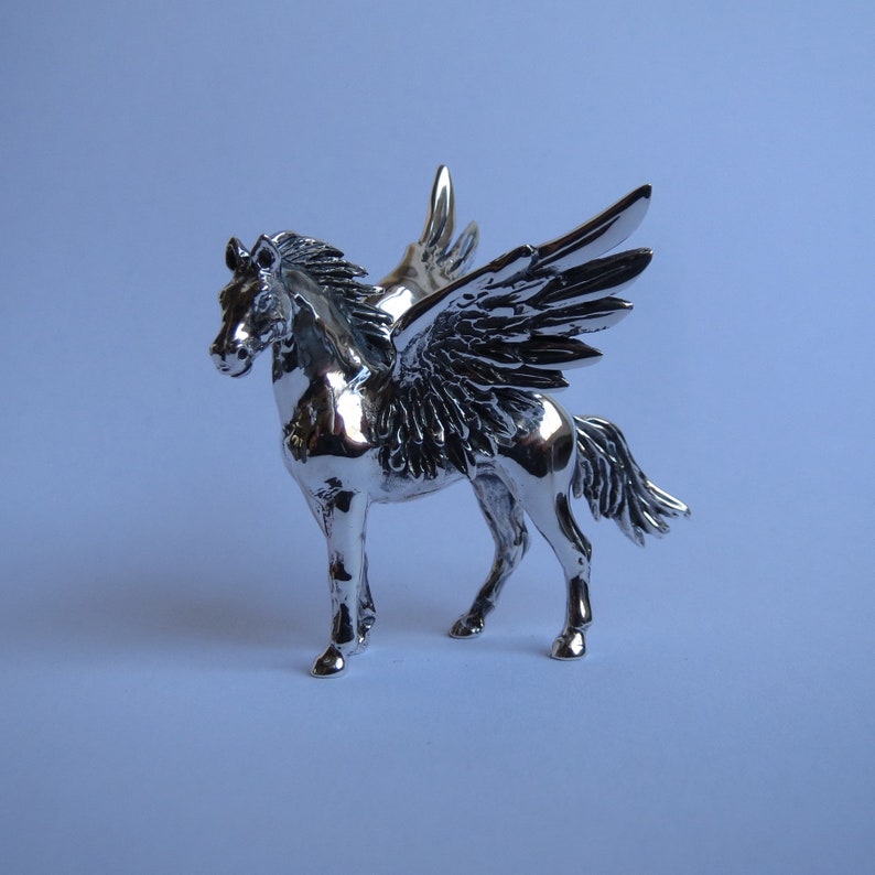 May include: A silver figurine of a winged horse, with detailed wings and a sleek, muscular body. The horse is standing on all four legs, with its head held high.