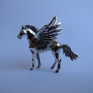 May include: A silver figurine of a winged horse, also known as a Pegasus, with a detailed sculpted design. The horse is standing with its wings spread out.