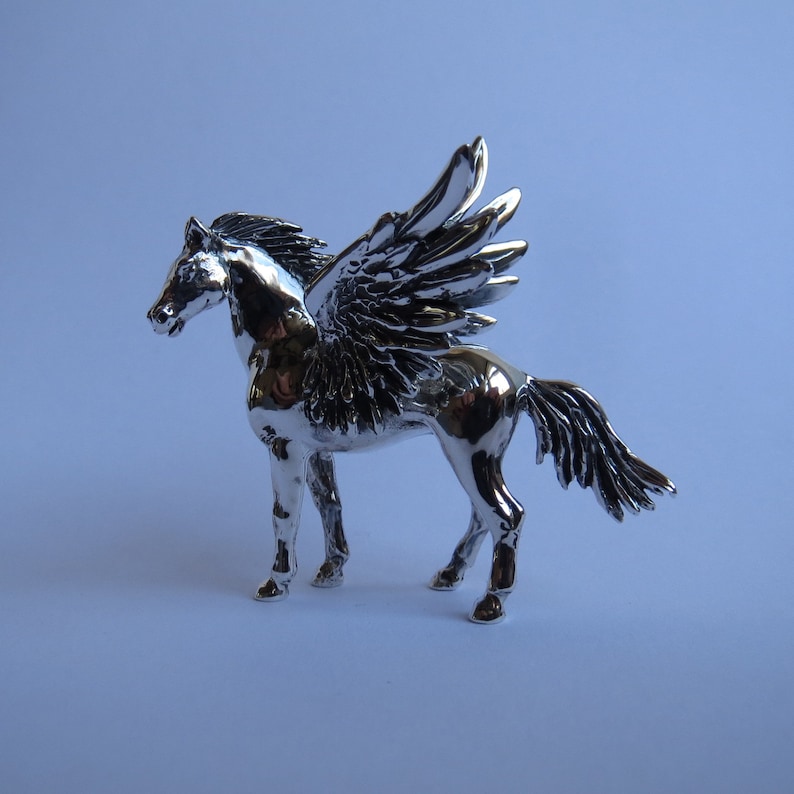 May include: A silver figurine of a winged horse, also known as a Pegasus, with a detailed sculpted design. The horse is standing with its wings spread out.