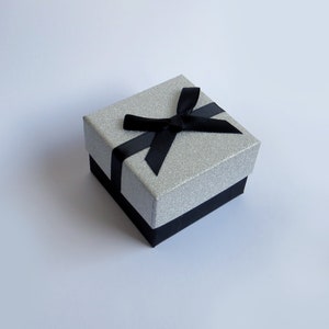 May include: A silver glitter gift box with a black satin ribbon and bow.