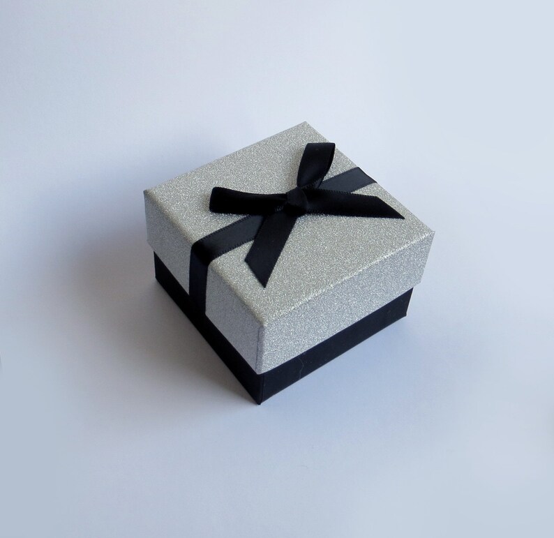 May include: A silver glitter gift box with a black satin ribbon and bow.