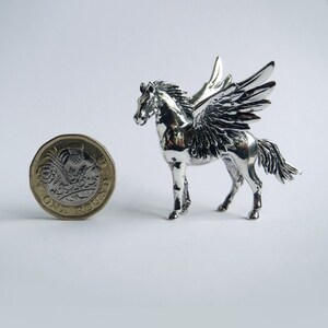 May include: A silver Pegasus figurine with wings outstretched. The figurine is about the size of a British one pound coin.