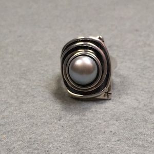 Peut inclure: Une bague en argent avec une grosse perle ronde grise sertie dans un motif tourbillonnant et textur&eacute;.