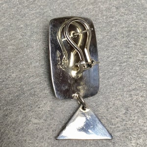 May include: Silver dangle earrings with a rectangular top and a triangular dangle. The earrings have a silver hook closure.